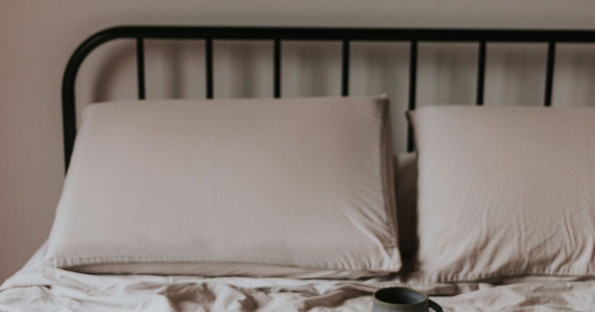 A calm, warm-toned bed with soft linens and a coffee mug in soft natural light