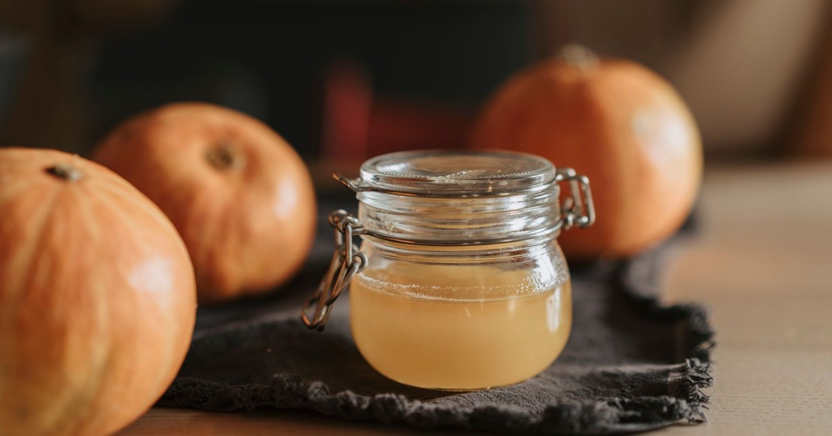 A glass jar of raw, cloudy apple cider vinegar on a wooden table