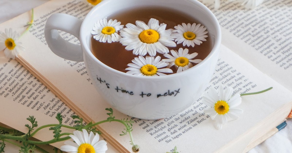 A mug of chamomile tea with chamomile flowers floating in it, beside fresh chamomile flowers