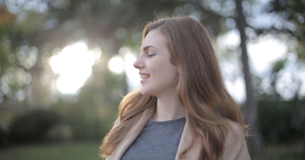 A woman outdoors in soft daylight with her eyes closed and a calm, contented expression