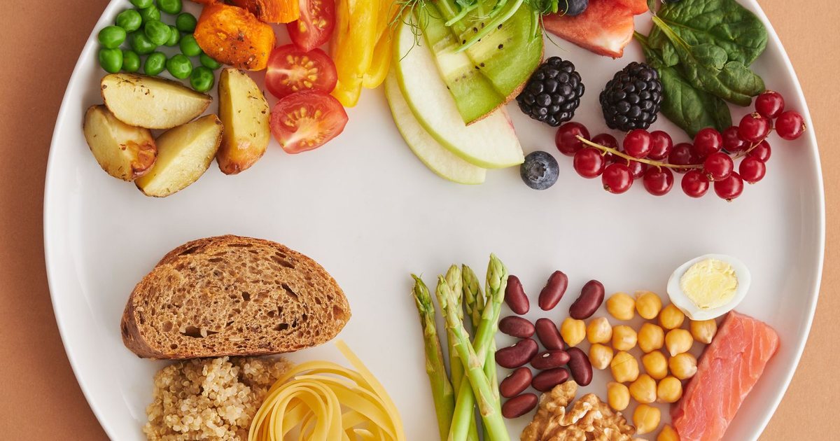An overhead flatlay of a plate of B-vitamin-rich whole foods including egg, salmon, beans, leafy greens, nuts, and whole grains