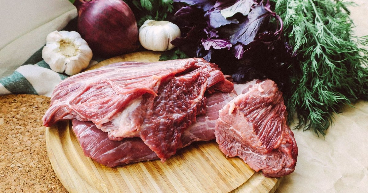Fresh raw red beef on a wooden cutting board with herbs and garlic