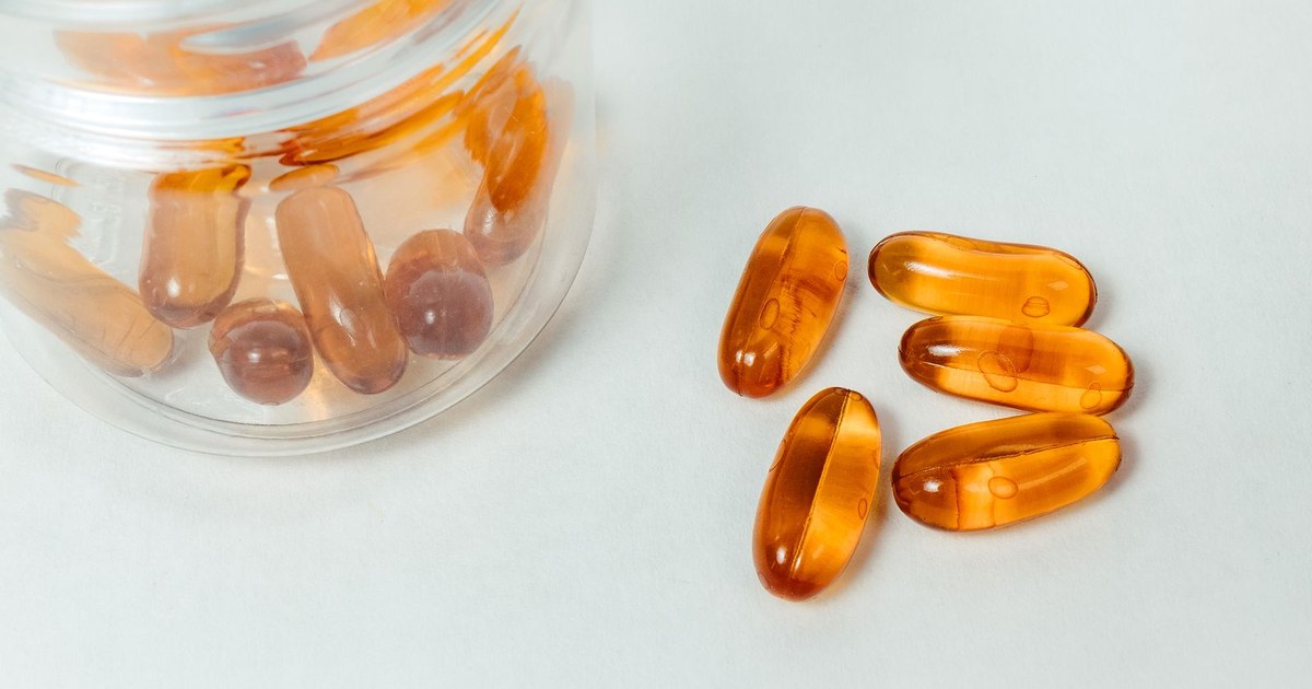 Golden supplement capsules beside a glass jar on a white surface