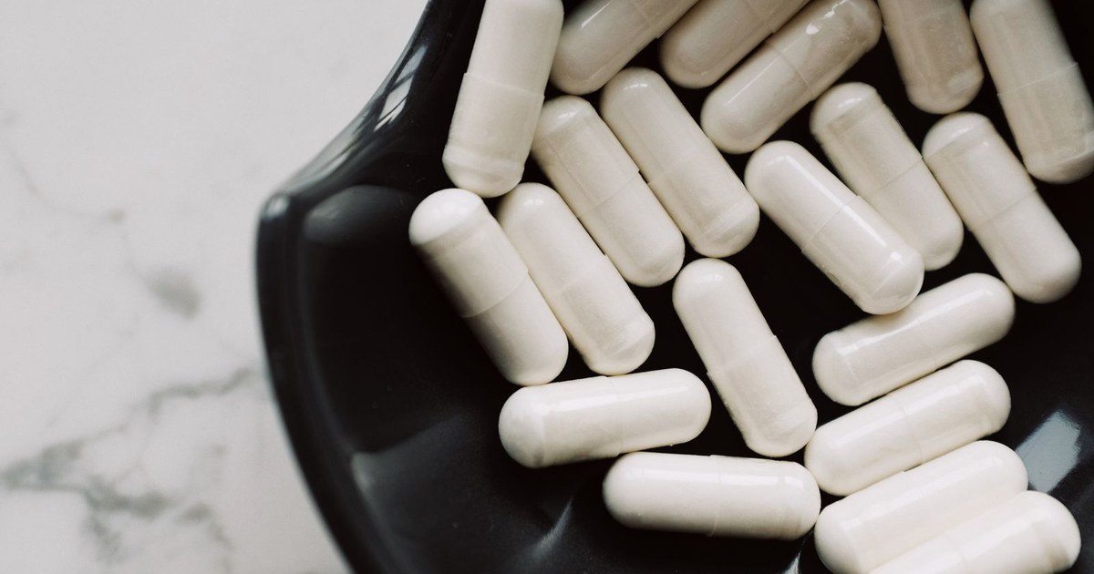 Large white capsules piled in a black bowl on a white marble surface
