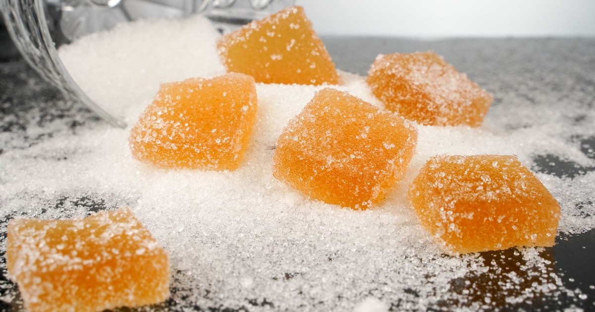 Sugar-coated orange jelly cubes resting on a pile of spilled white granules from a tipped glass jar