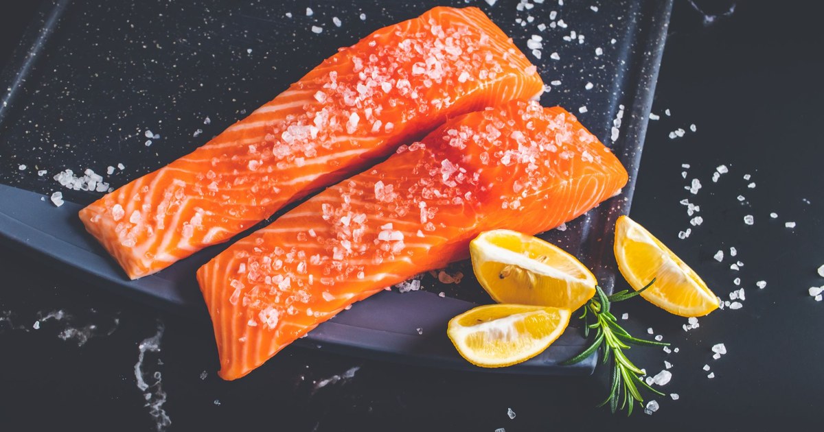 Fresh salmon fillets with lemon, salt, and rosemary on a dark surface