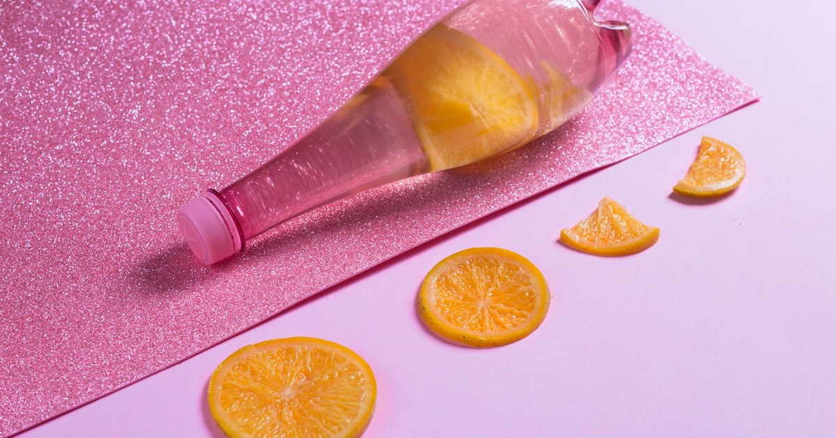 A pink-tinted drink bottle with orange slices on a pink glitter background