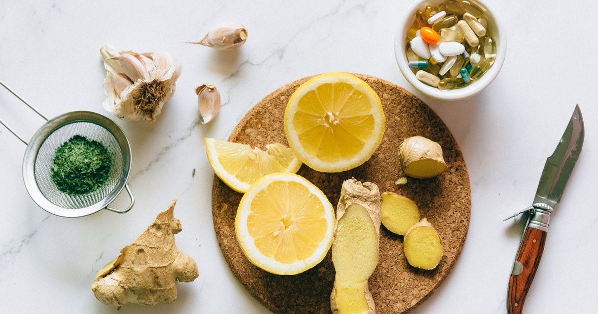 Flat lay of lemon slices, fresh ginger, garlic and a small bowl of supplement capsules on a marble counter