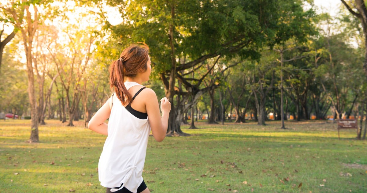 A woman jogging in a sunny green park at golden hour