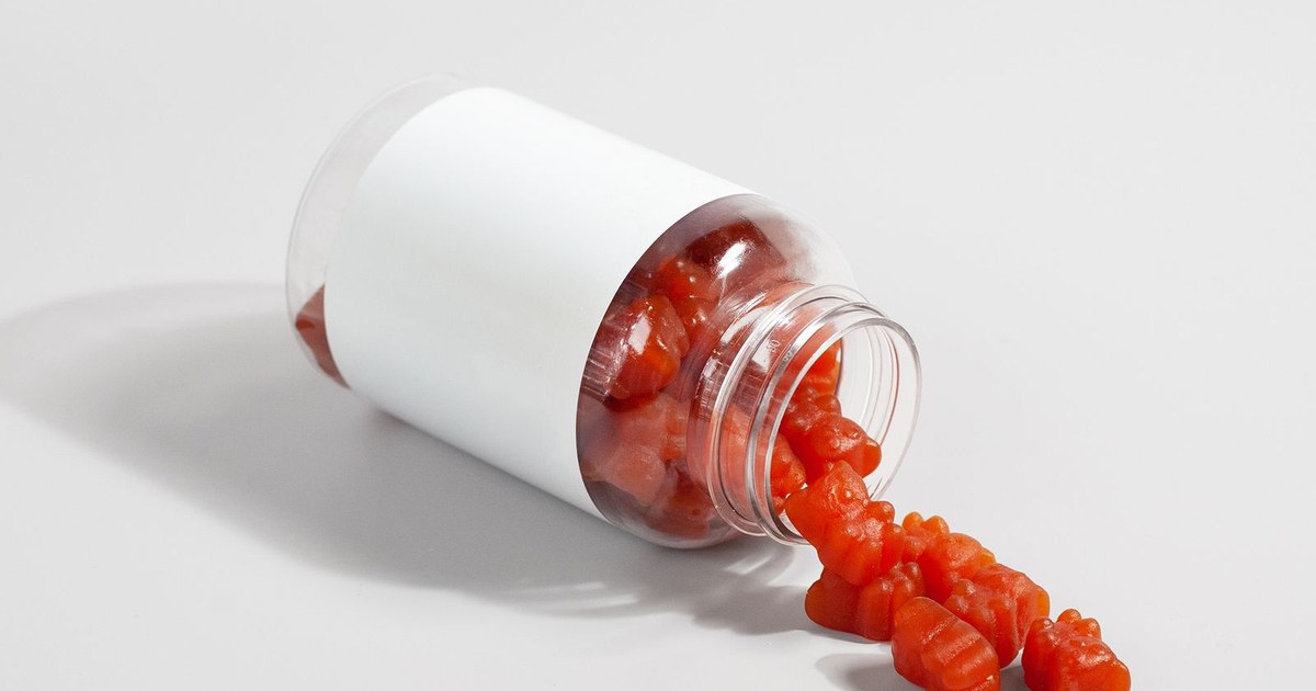 Orange gummy bear vitamins spilling from a tipped white bottle onto a bright white surface
