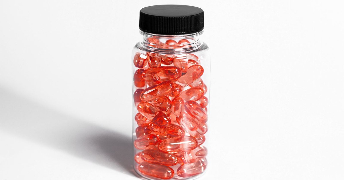 A clear bottle of red-orange omega-3 softgel capsules on a white background