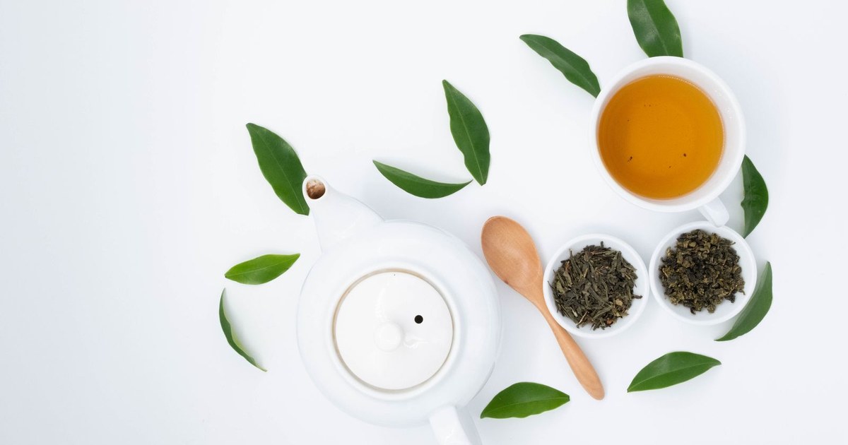 A cup of green tea with a teapot and fresh green tea leaves