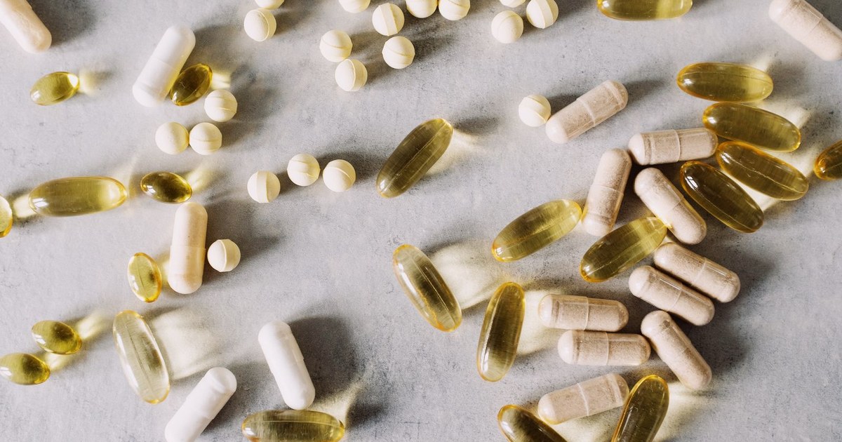 An assortment of supplement capsules, softgels, and tablets on a marble surface