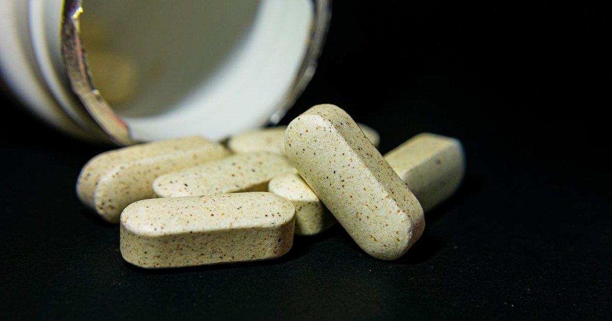 Supplement tablets spilling from a bottle on a dark surface