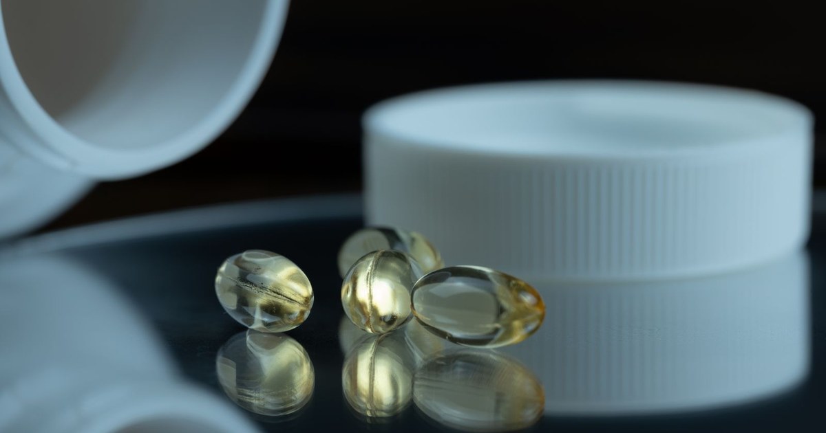 Golden softgel capsules beside an open white supplement bottle on a dark reflective surface