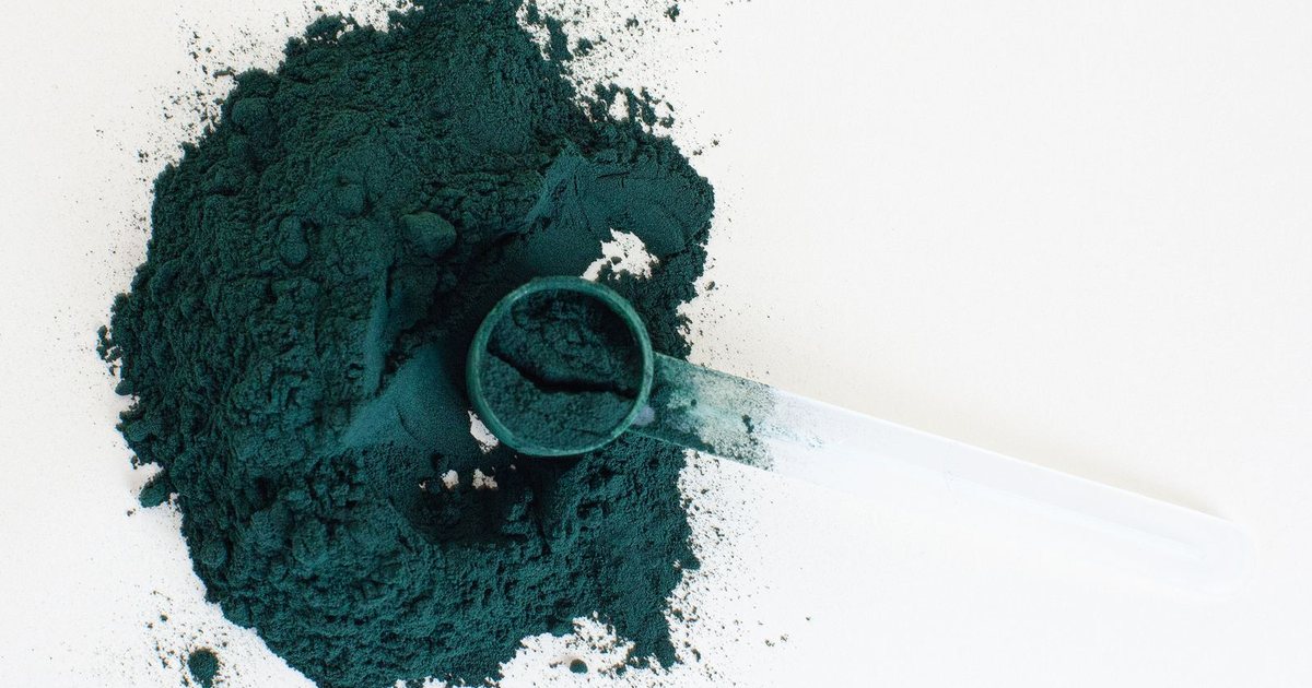 A mound of deep blue-green spirulina powder with a plastic measuring scoop resting on a clean white surface
