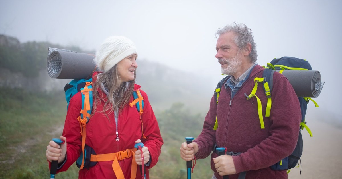 Smiling senior couple hiking outdoors with trekking poles and backpacks on a misty trail