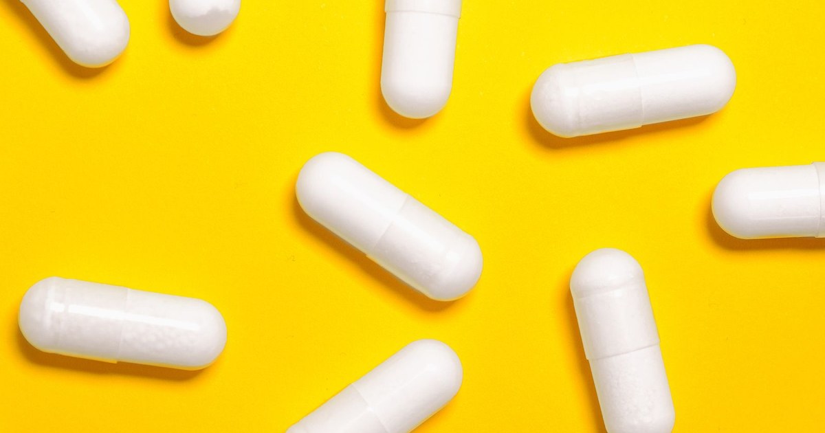 White supplement capsules scattered across a bright yellow background