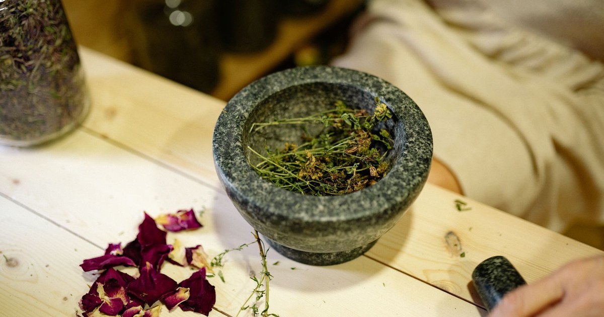A stone mortar and pestle with dried herbs on a wooden table