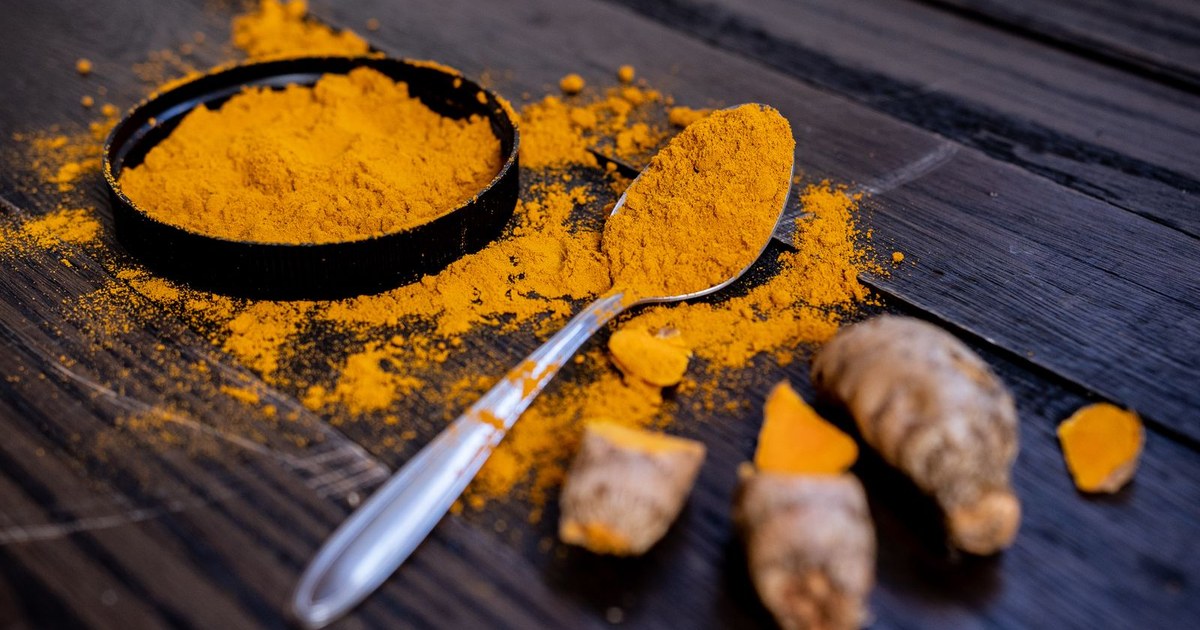 Ground turmeric powder and fresh turmeric root on a wooden surface