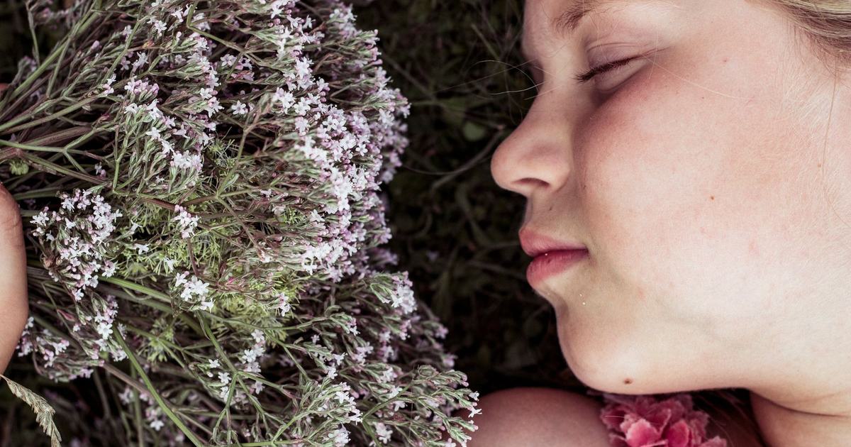 A young woman sleeps peacefully with her eyes closed while resting beside a bundle of pink and white valerian flowers