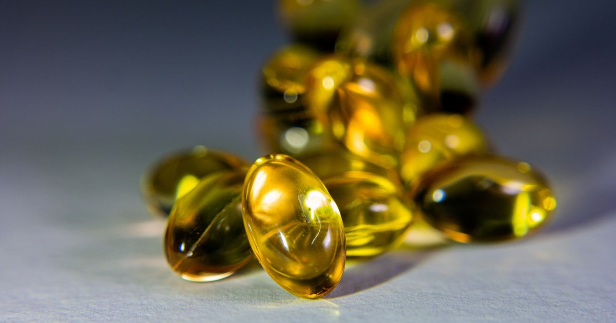 Golden vitamin D softgel capsules spilling onto a pale surface