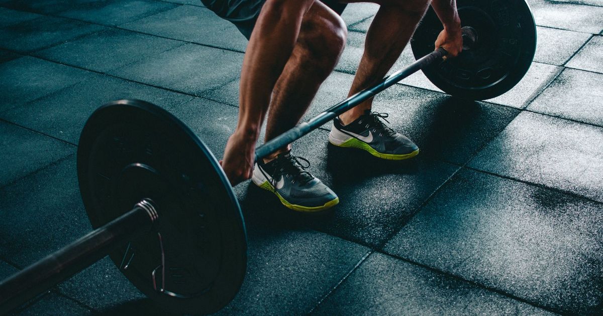 A person crouches on a dark gym floor gripping a loaded barbell just before a heavy lift