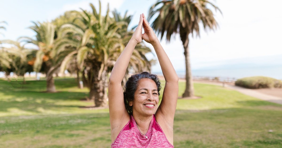 Active older woman practicing yoga outdoors in a sunny park, illustrating comfortable joint mobility and flexibility