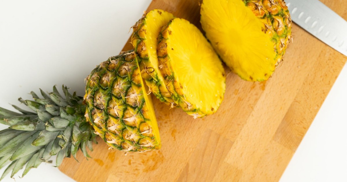 A pineapple cut into thick rounds on a wooden cutting board beside a kitchen knife