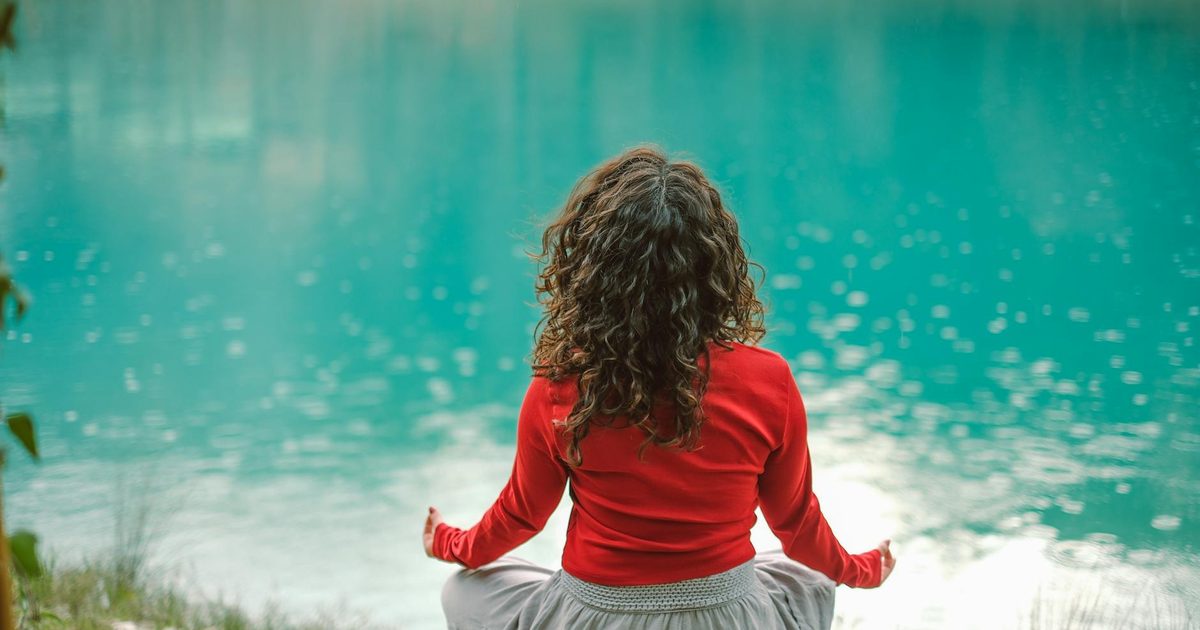 A woman meditating calmly beside a tranquil lake