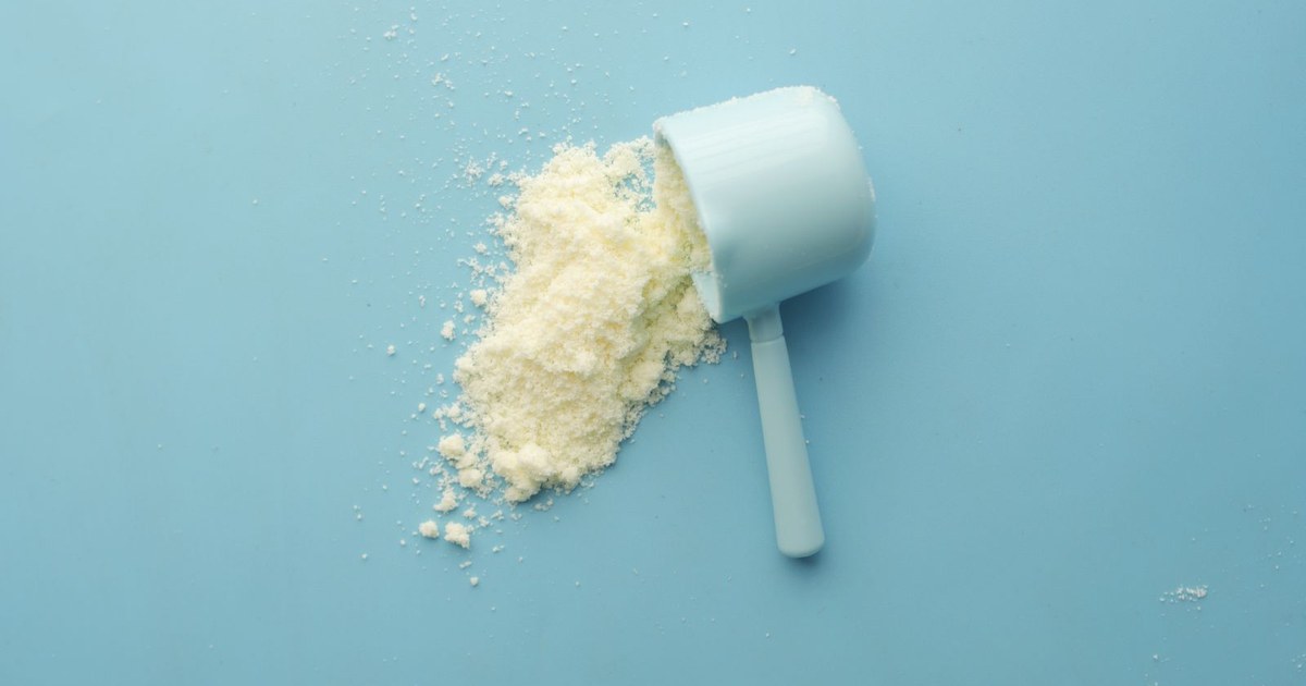 White supplement powder spilling from a measuring scoop on a bright blue surface