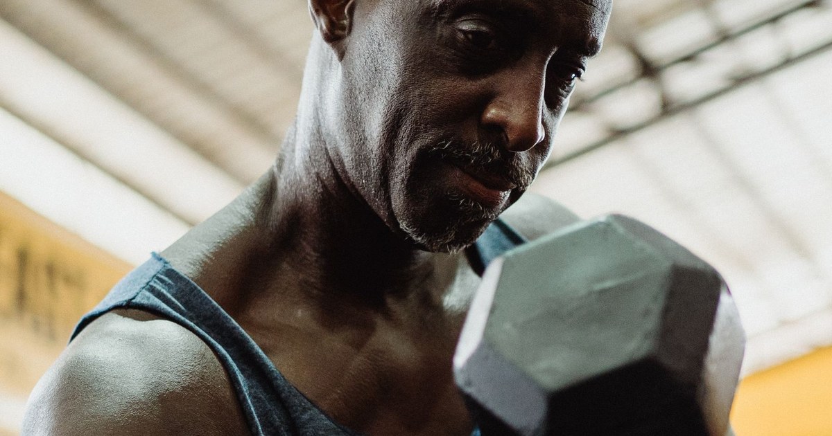 An older man in a tank top doing a dumbbell curl in a gym, focused on the weight, strength training to preserve muscle