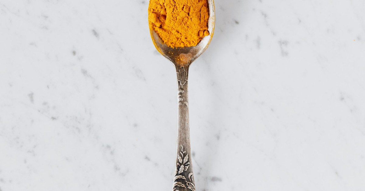 A silver spoon heaped with golden turmeric (curcumin) powder on a clean white marble surface