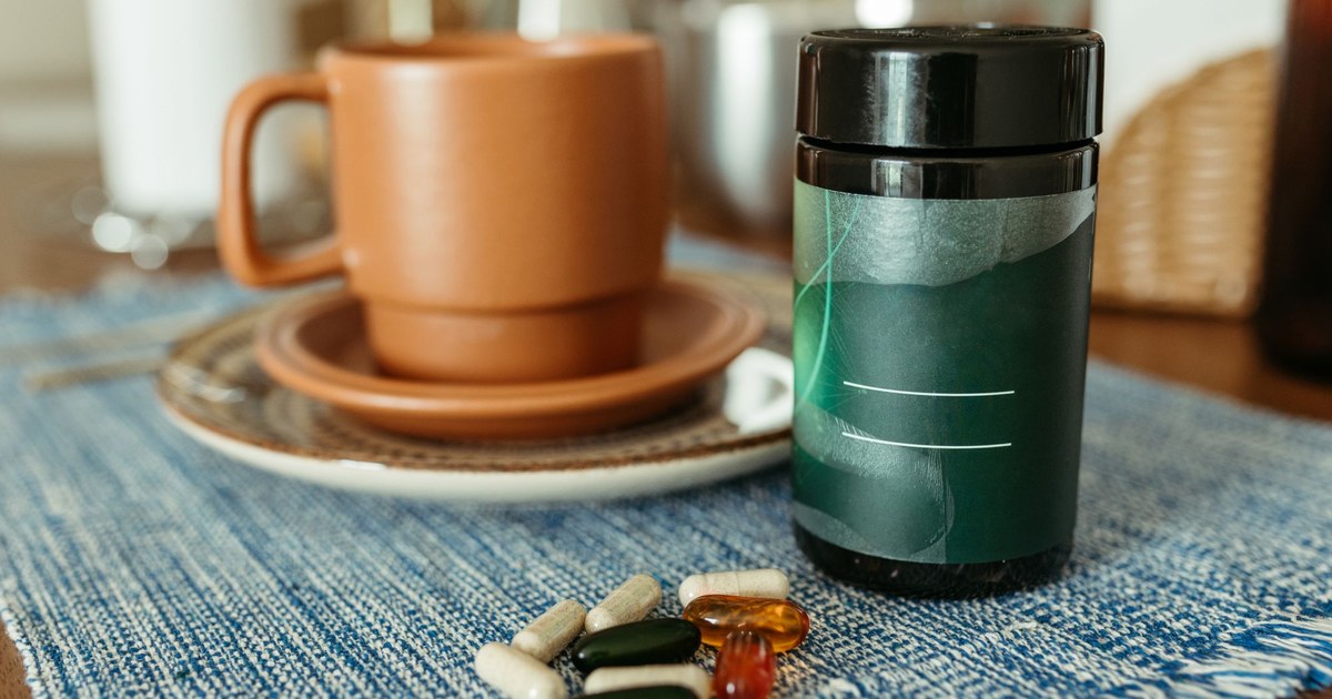 A cup of coffee beside a supplement jar and a pile of capsules