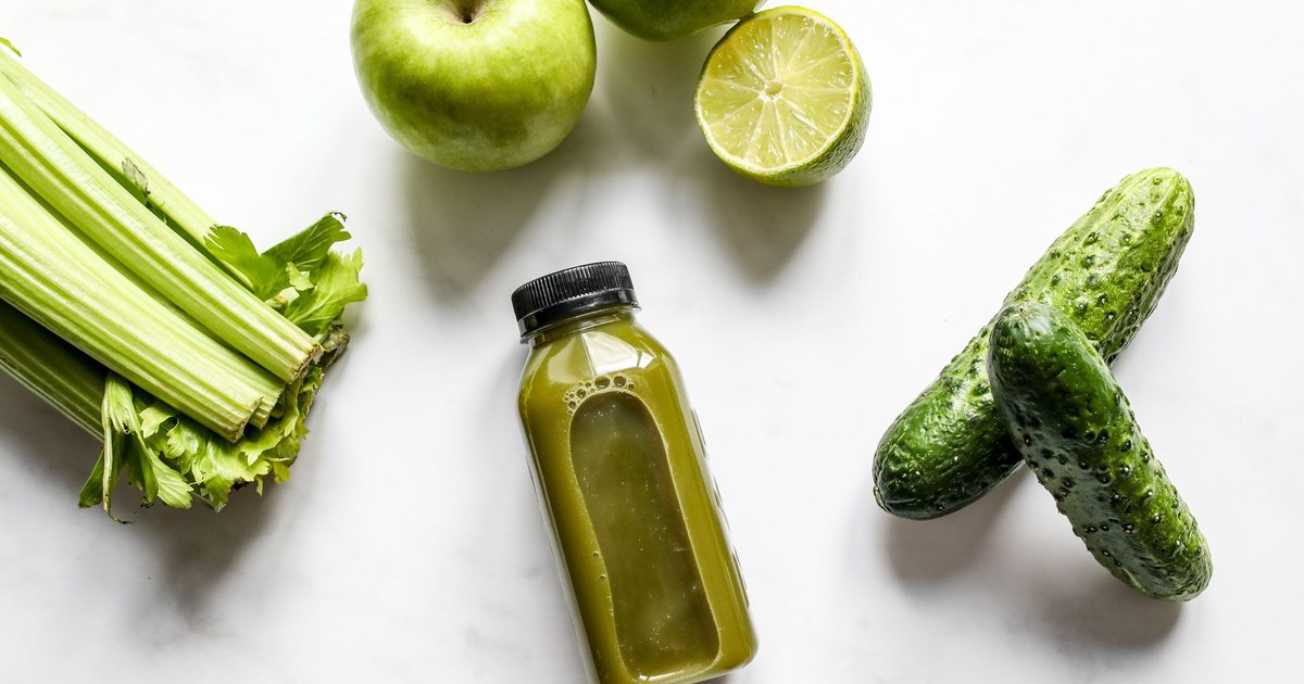 A green juice with celery, apple, lime, and cucumber on a marble surface