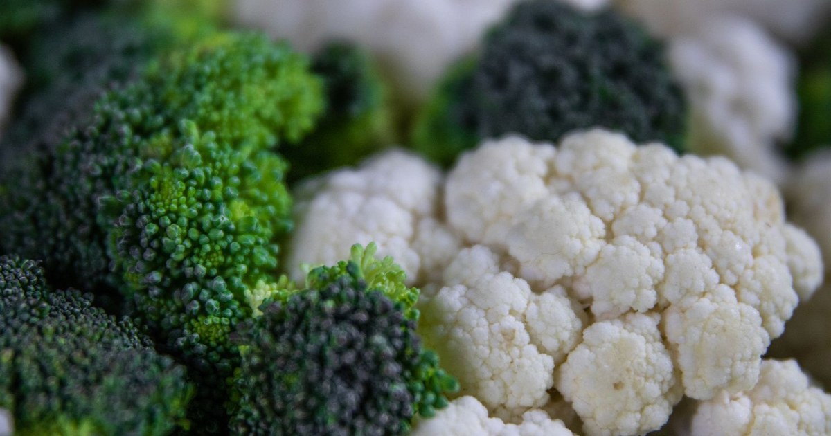 A close-up of fresh green broccoli florets beside a white cauliflower head