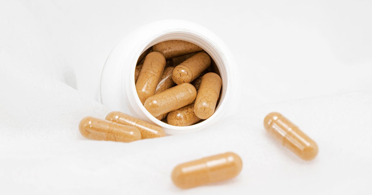 Amino acid supplement capsules spilling from a white jar