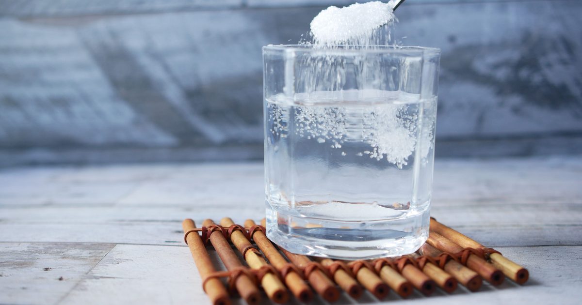 A scoop of white powder dissolving in a clear glass of water
