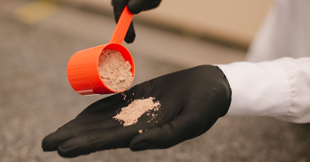 A scoop of colored pre-workout powder being measured out over a gym floor