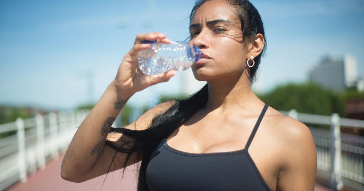A woman drinking bottled water outdoors after a workout