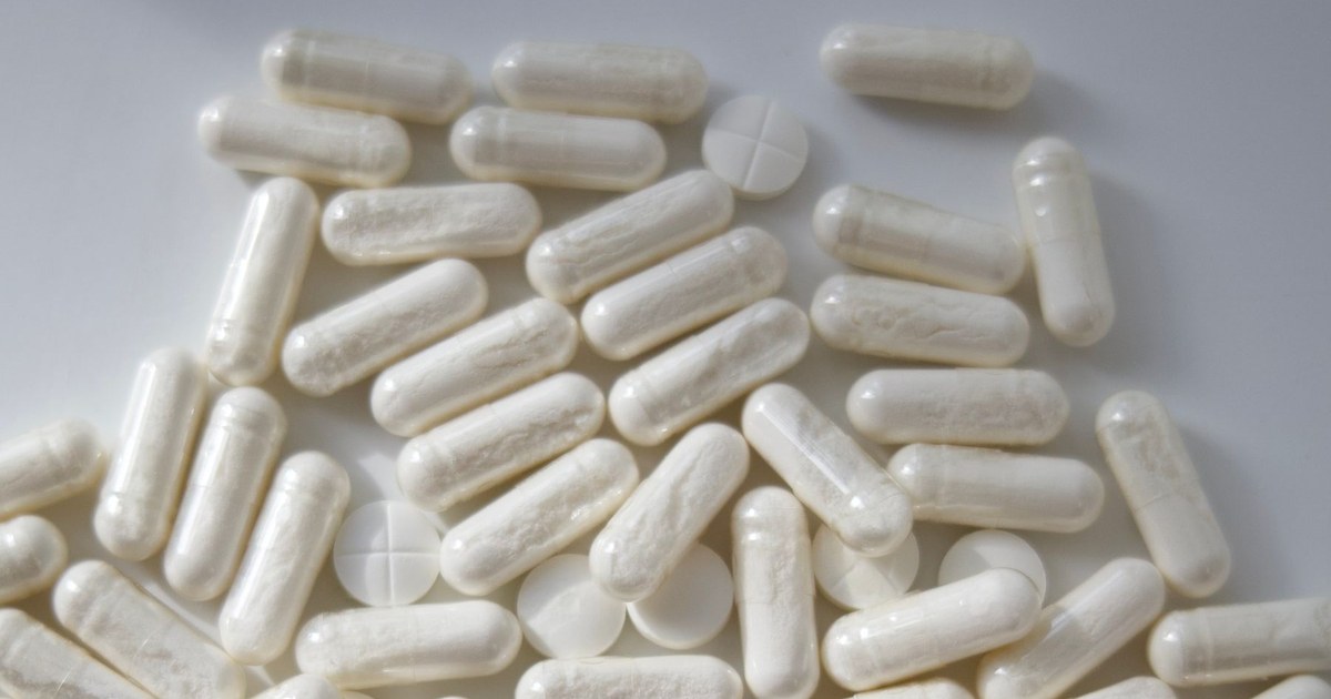 A scattered pile of plain white capsules and round tablets on a pale gray surface