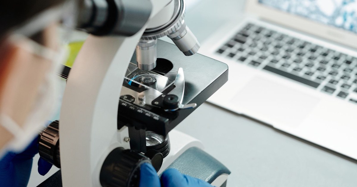 A researcher in protective gear examines biological samples through a microscope in a modern laboratory