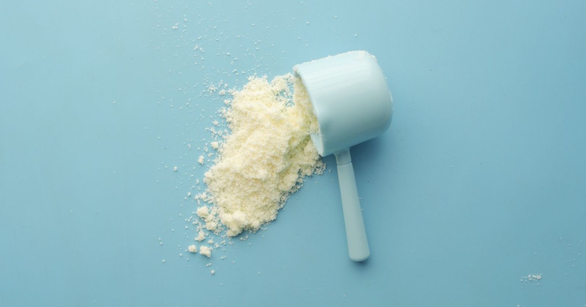 A light blue scoop tipped on its side with pale powder spilling onto a blue surface