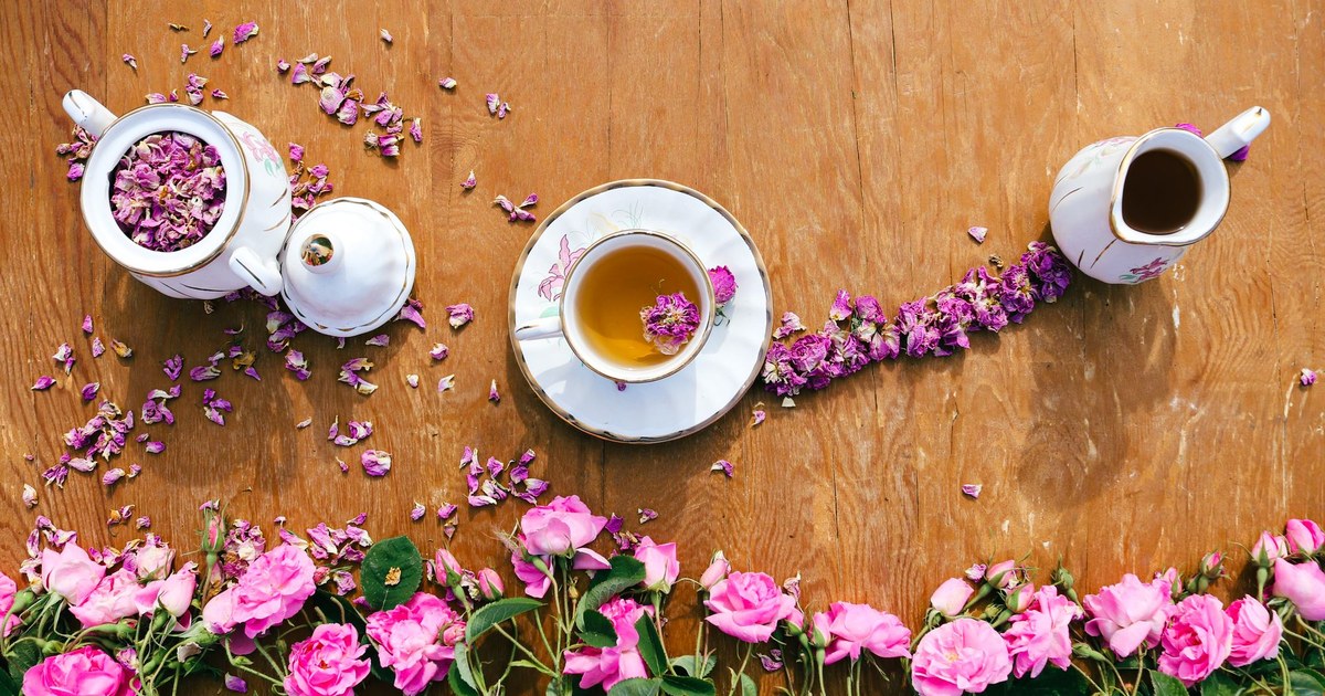 A rose tea setting with teapot, cup, and fresh pink roses on a wooden table