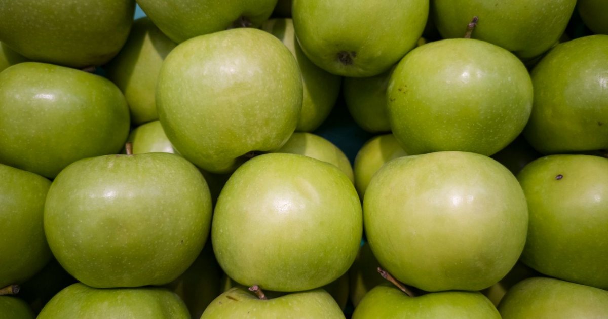 A close-up of bright green apples stacked together