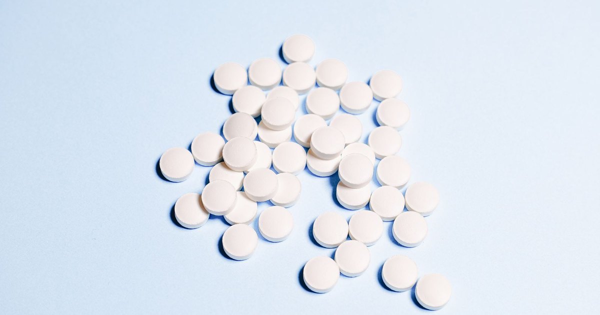 A scattered pile of round white tablets on a light blue surface