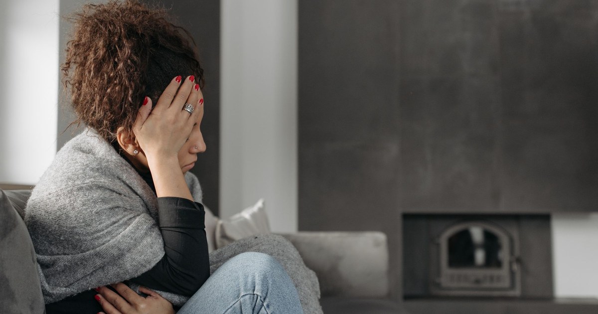 A woman sitting on a couch with a hand pressed to her forehead