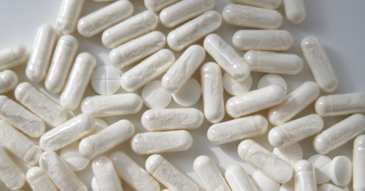 A pile of white supplement capsules on a light surface