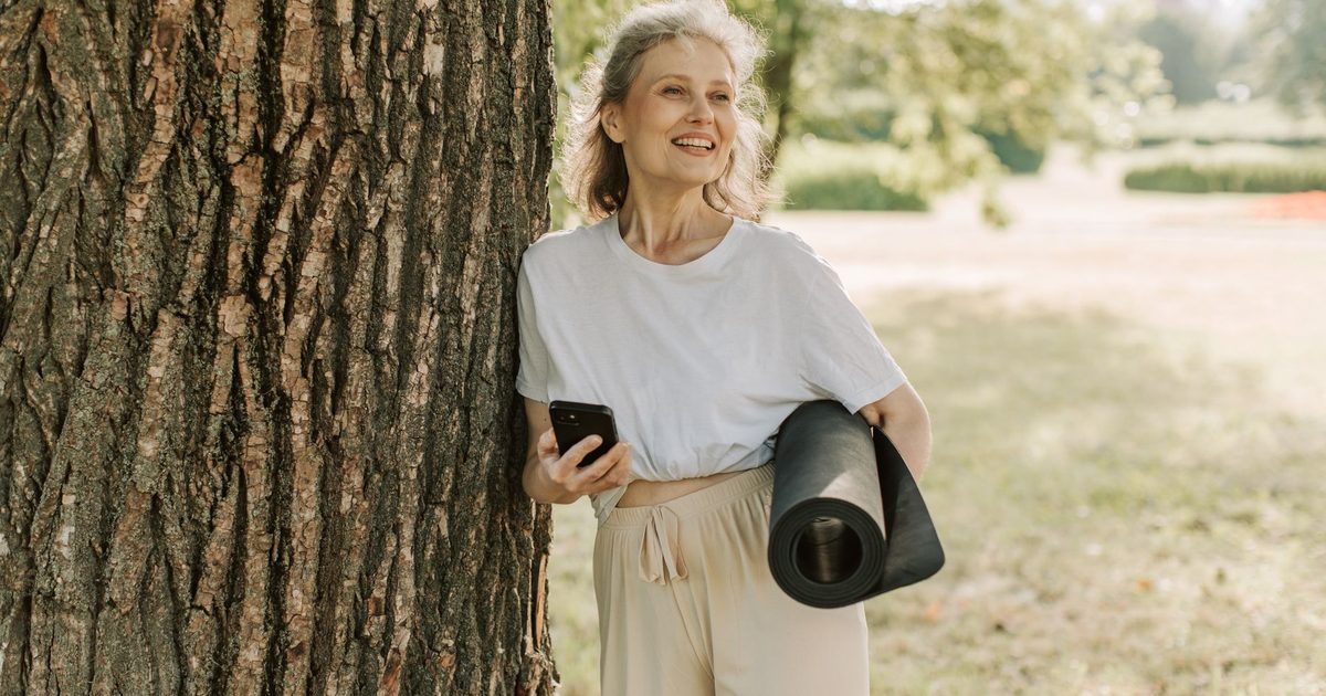 An active healthy older woman holding a yoga mat in a park