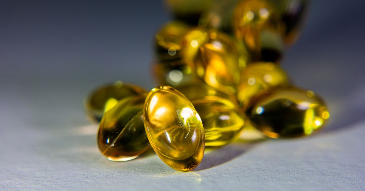 Glowing golden fish oil softgels clustered on a pale gray surface